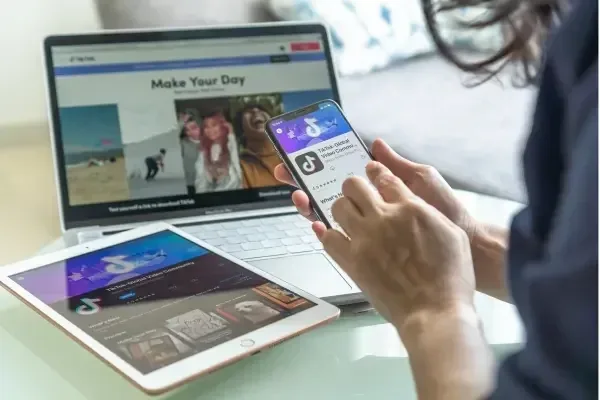 Someone holding an Iphone wth TikTok open for marketing purposes with iPad and MacBook also in front of them.